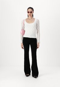 Weißes Spitzenoberteil mit langen Ärmeln, schwarze Schlaghose, rosa Handtasche und rosa Sonnenbrille. Glatte Textur und taillierter Schnitt mit rundem Halsausschnitt.