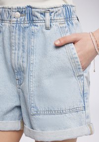 Bermuda in denim azzurro chiaro con vestibilità rilassata, orli arrotolati, vita elastica e tasche frontali. Tessuto stonewashed con leggera scoloritura.