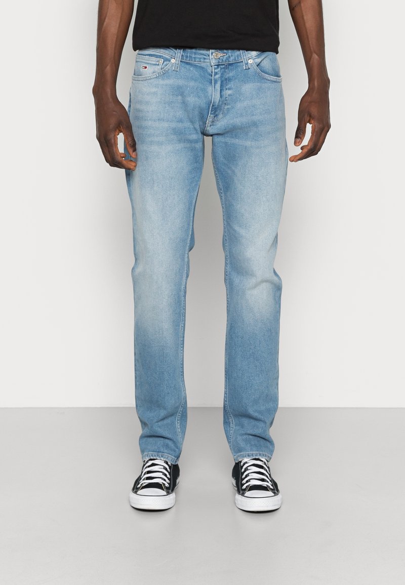 Světle modré džíny s rovnými nohavicemi, které mají design s pěti kapsami a stříbrné kovové prvky. Vydány s černými teniskami.