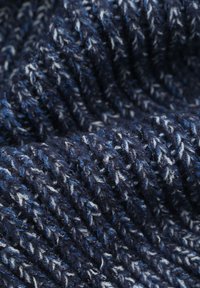 Gebreide stof in donker marineblauw met lichtblauwe en witte spikkels. Gestructureerde, dikke strengen creëren een zacht, warm uiterlijk.