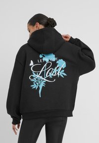 Felpa nera con taglio ampio e cappuccio grande. Sul retro presenta una scritta grafica blu "LET'S GET LOST" con dettagli botanici e farfalle.