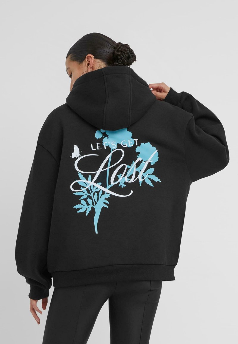 Felpa nera con taglio ampio e cappuccio grande. Sul retro presenta una scritta grafica blu "LET'S GET LOST" con dettagli botanici e farfalle.