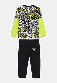 Zweiteiliges Outfit bestehend aus einem schwarzen Langarmshirt mit Neonakzenten und auffälligen grafischen Prints, kombiniert mit schwarzen Jogginghosen aus Fleece mit Taschen.