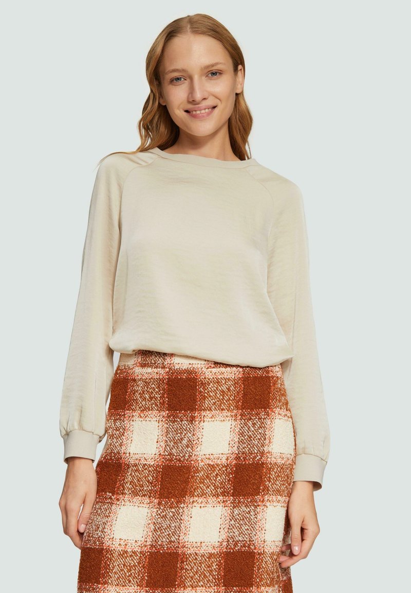 Beige Langarmoberteil mit Raglanärmeln, kombiniert mit einem karierten Rock, der braune und cremefarbene Quadrate aus einem strukturierten Stoff zeigt.