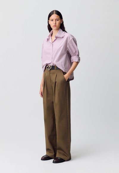 Camisa de algodón a rayas con mangas enrolladas, combinada con pantalones marrones de talle alto con pliegues y una hebilla de cinturón decorativa.