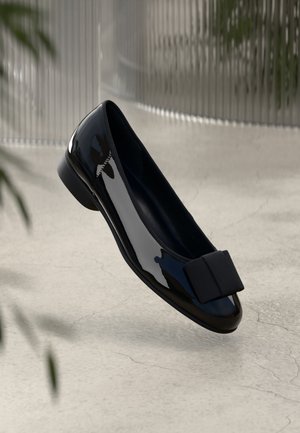 Czarna balerina z lakierowanej skóry ze zaokrąglonym noskiem, teksturowaną kokardą z przodu oraz niskim, solidnym obcasem. Gładkie wykończenie, minimalistyczny design.