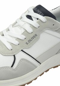 Fehér és szürke sneaker, amely velúr és hálós anyagokból készült, lapos fehér fűzőkkel és fekete sarkú kiemeléssel. A márkázás az oldalon található.
