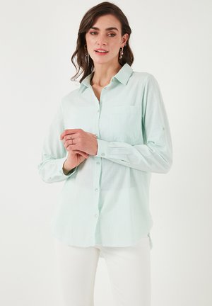Light mint green button-up shirt with a pocket, collar, and long sleeves, made of a soft, textured fabric; features a curved hem.