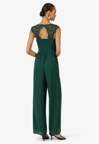 Emerald green jumpsuit with a lace-accented bodice, smocked waist, and wide-leg design. Open back detail adds visual interest.