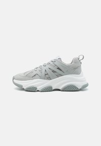 Baskets de sport gris clair avec une tige en maille et en daim, une semelle intermédiaire blanche épaisse, une semelle en caoutchouc texturé et une languette au niveau du talon.