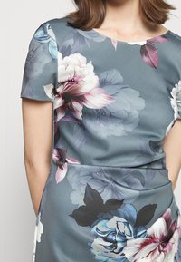 Robe fleurie à manches courtes, à fond gris, avec de grands motifs de pivoine et de rose en rose, blanc et bleu, et un col rond.