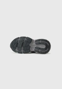 Suela de zapatilla de goma negra con un patrón de textura, que incluye surcos y tacos para tracción. Cuenta con una entresuela gris.