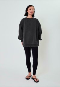 Dunkelgrauer, übergroßer Sweatshirt mit überschnittenen Schultern, mit pinker Stickerei, kombiniert mit schwarzen Leggings und schwarzen Flip-Flops.