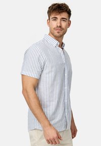 Camisa de botones de manga corta en azul claro y rayas verticales blancas, hecha de tela ligera con un cuello clásico y un ajuste estándar.