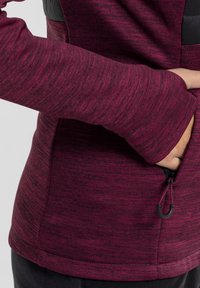 Maroon pullover with long sleeves, featuring a textured knit design and a zippered pocket on the side. Smooth fabric with contrasting accents.