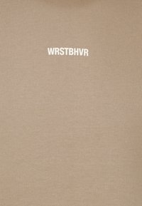 Béžová přiléhavá košile z žebrované látky, uprostřed s bílým nápisem "WRSTBHR". Hladká textura s neformálním designem.