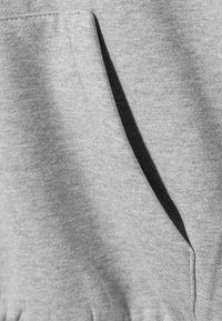 Pilkos spalvos džemperio su gobtuvu audinys, kuriame matoma didelė priekinė kišenė, minkšta tekstūra ir subtilus blizgesys, su siūlių detalėmis matomomis palei kraštus.