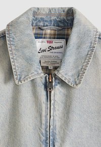 Φωτεινή γαλάζια τζιν μπουφάν με κλείσιμο με φερμουάρ, μυτερό γιακά και καρό φόδρα. Διαθέτει ετικέτα με λογότυπο και πληροφορίες φροντίδας.