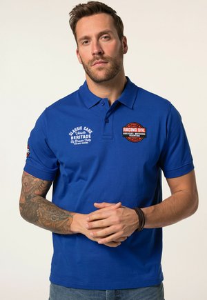 Modrá polo triko vyrobené z bavlny, s vyšívanými logy na hrudi a rukávu, krátkým rukávem a klasickým designem límce.
