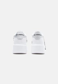 Białe platformowe trampki z teksturowanym srebrnym obcasem. Ozdobione logo "KARL LAGERFELD" oraz dekoracyjnymi łańcuszkami po bokach.