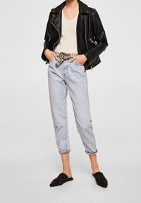 Giacca da biker in pelle nera, top in maglia crema, jeans a vita alta azzurri, cintura in stampa serpente beige e scarpe slip-on nere con decorazioni.