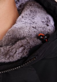 Czarna kurtka z miękkim szarym futerkiem w środku i pomarańczowym sznurkiem ściągającym przy kołnierzu, częściowo zapięta.