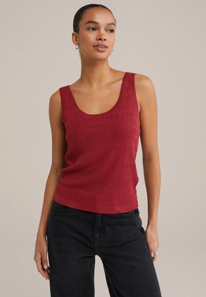 Débardeur rouge à côtes avec des bretelles larges, un col arrondi et une coupe décontractée, associé à un jean noir taille haute. Fond uni.