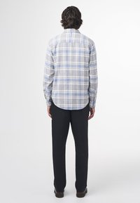 Pánská košile s dlouhým rukávem v světle šedé barvě s modrým kostkovaným vzorem, košile s knoflíkovým límečkem, zakřiveným zakončením a černé kalhoty. Tkanina vypadá hladce.