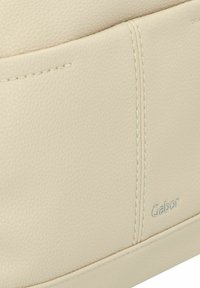 Borsa a mano in pelle beige con superficie texturizzata, dettagli di cucitura e logo metallico "Gabor" su un lato. Design compatto e minimalista.