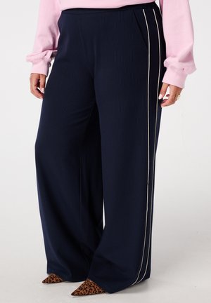 Marineblauwe wijde broek met verticale strepen, voorzien van zijzakken en een contrasterende witte bies. Zacht, gestructureerd materiaal. Leopardenprint hakken.