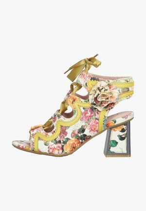 Sandalia de tacón abierta con patrón floral, ribete amarillo en forma de ondas, lazos en el tobillo, flor decorativa de tela y tacón cuadrado.