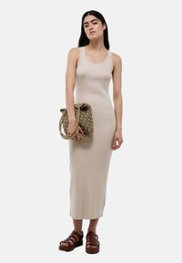 Robe débardeur beige côtelée de longueur midi. Le modèle tient un sac en toile de couleur tan avec une poignée nouée. Sandales à plateforme marron à lanières.