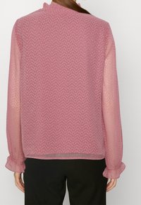 Blusa trasparente rosa con motivo a pois testurizzati, maniche lunghe e polsini arricciati. Tessuto morbido e vestibilità leggermente ampia.
