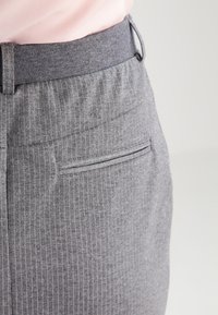 Jupe grise à fines rayures avec taille élastique et une poche arrière discrète. Texture douce, coupe ajustée, et couleur neutre.