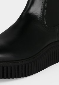 Botte en cuir noir avec semelle plateforme épaisse à rainures et panneau latéral élastique pour un enfilage facile.
