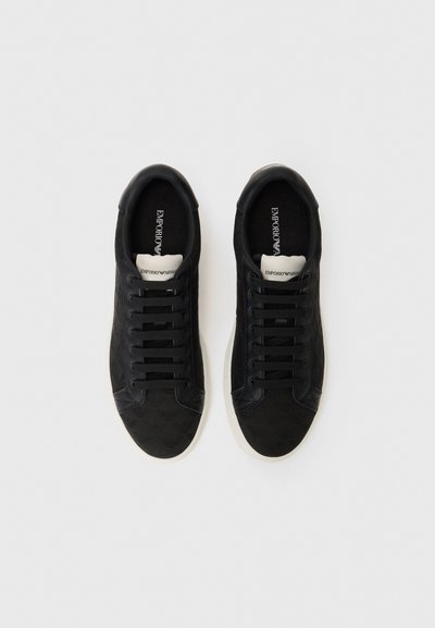 Baskets en suède noir avec un design texturé, dotées de lacets plats, d'un embout rond et d'une semelle en caoutchouc blanche. Marque à l'intérieur visible.