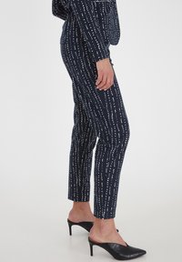 Pantalones de patrón navy en corte slim, con rayas verticales blancas. Hechos de una tela suave, combinados con tacones negros puntiagudos.