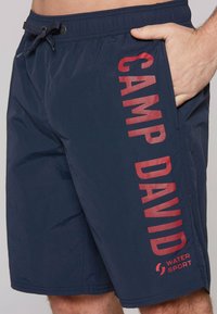 Námornícke modré plavky z ľahkej tkaniny s elastickým pásom, s nápisom "CAMP DAVID" v červenej farbe a bočnou vreckom.
