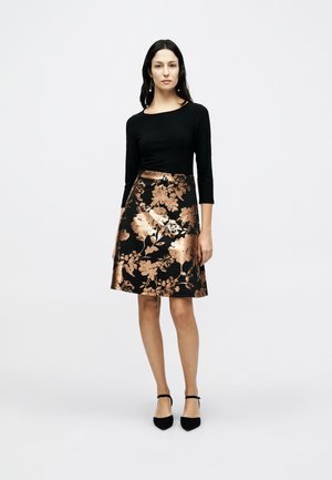 Μαύρο μακρυμάνικο τοπ σε συνδυασμό με φούστα μήκους μέχρι το γόνατο, διακοσμημένη με μεταλλικά ροζ χρυσά λουλουδάτα μοτίβα και λεία υφή. Φορεμένο με μαύρα τακούνια.