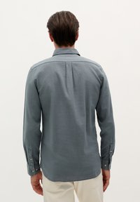 Grijze button-up shirt met lange mouwen, een achterkant met yoke-detail en een zachte textuur. De manchetten hebben knoopsluitingen.