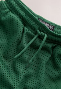 Grüne Sportshorts aus atmungsaktivem Mesh-Stoff, mit einem Kordelzugbund und einem oben aufgenähten Etikett mit der Aufschrift "SPORTY".