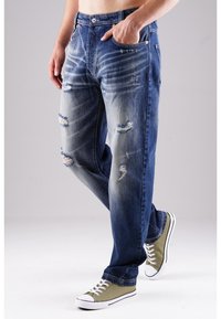 Helle blaue Denim-Jeans mit verwaschenen Details, einschließlich Rissen und Ausbleichungen. Geraffte Passform, kombiniert mit grünen Sneakers.