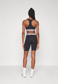 Ensemble de sport noir composé d'un crop top sans manches et de shorts mi-cuisse, avec une taille élastique blanche de marque et une texture de tissu lisse.