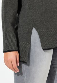 Sweater en tricot gris foncé avec des bords côtelés et des fentes sur les côtés. Le bas est orné d'un accent noir contrastant. Texture lisse visible.