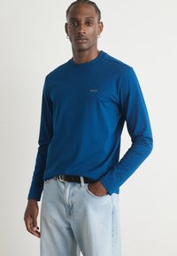 Langermet blå bomullskjorte med rund hals og subtilt brodert 'BOSS'-logo på brystet, kombinert med lyseblå jeans.