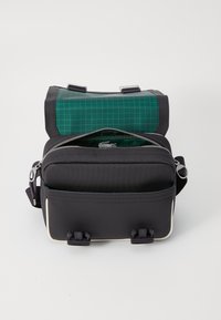 Black backpack with a green grid-patterned top flap. Features silver zippers, adjustable straps, and a front pocket with hardware accents.