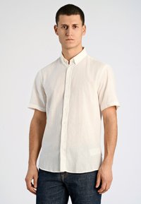 Kortärmad skjorta med knappar i ljus krämfärg, gjord av linne. Har en klassisk krage, subtil textur och rak fåll. Matcher med mörka jeans.