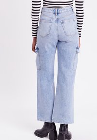 Lichtblauwe high-waisted jeans met een brede pijp, voorzien van twee zijvakken voor cargo en achterzakken, gemaakt van denim stof.