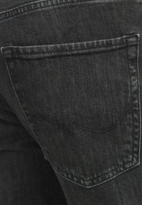 Svarta denimjeans med en bakficka som har subtila sömnadsdetaljer. Texturen ser slät ut med en svag glans.