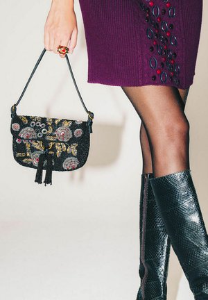 Schwarze Perlenhandtasche mit Blumenstickerei, Quasten-Detail, goldener Hardware und abnehmbarem Riemen, kombiniert mit einem lila gerippten Kleid und kniehohen Stiefeln.